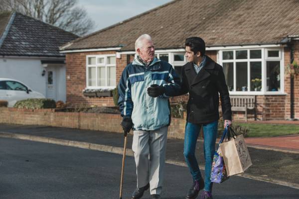 A carer helping man across the road with shopping
